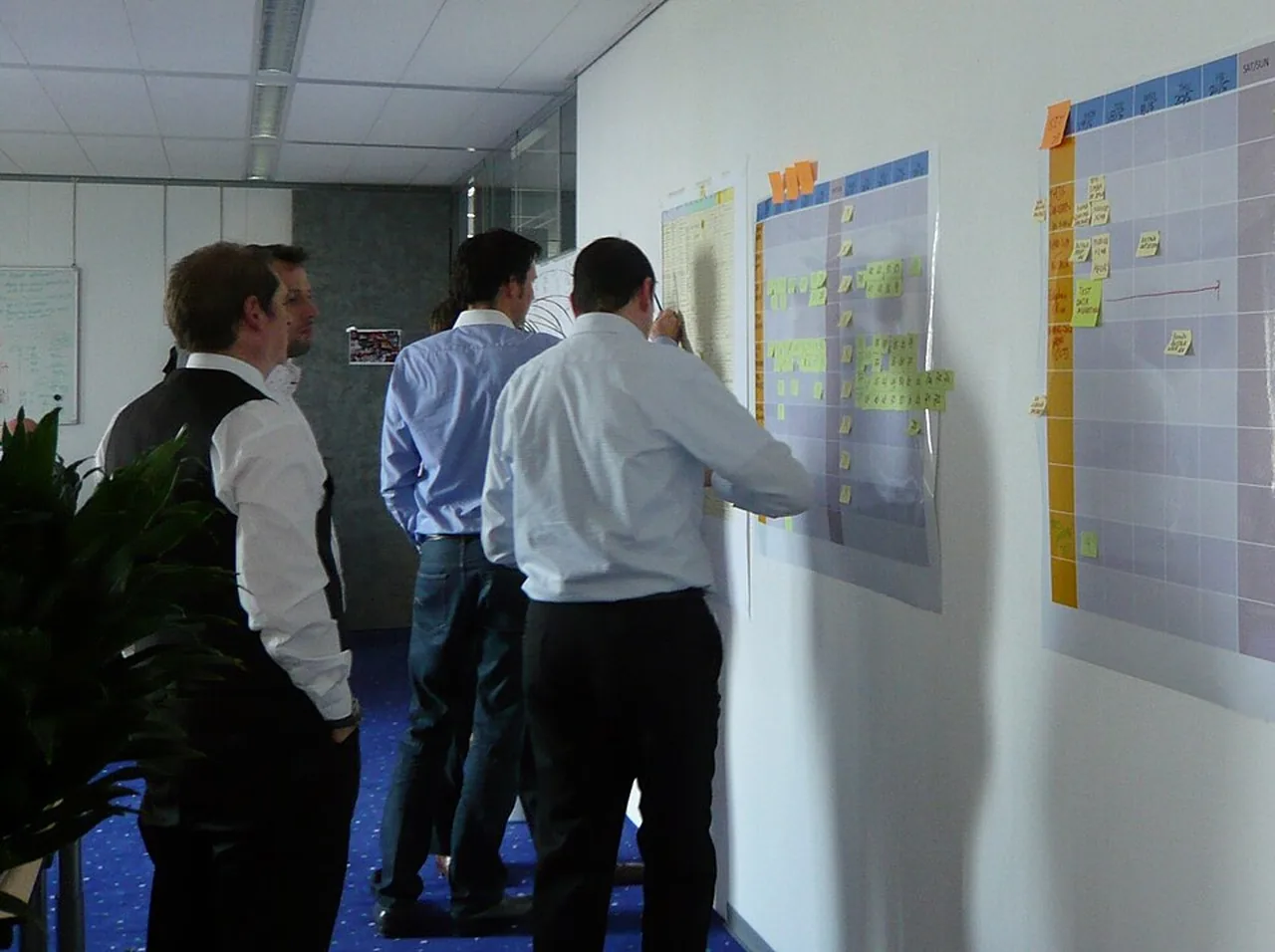 Four people reviewing task cards on large wall-mounted planning boards.