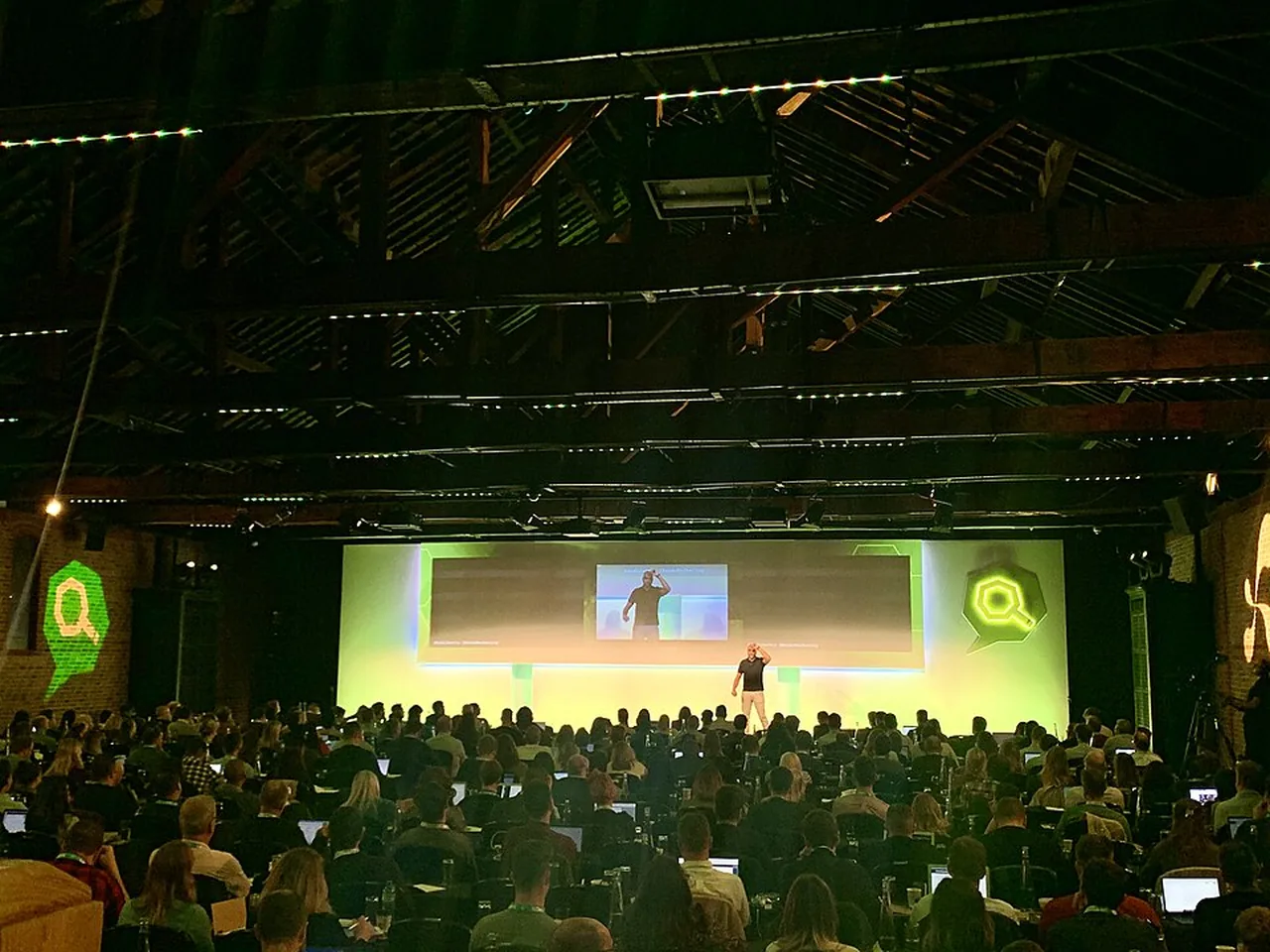 A presenter speaks on a lit stage to a large seated audience at a marketing conference in London.